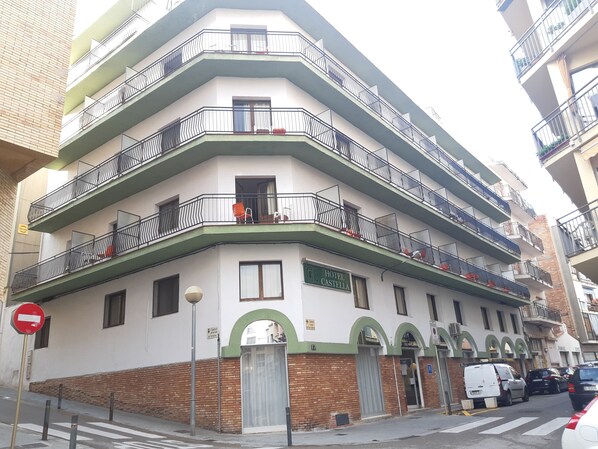 Un hotel de varios pisos con balcones, un arco de entrada verde y un letrero que dice 'Hotel Castellá'.