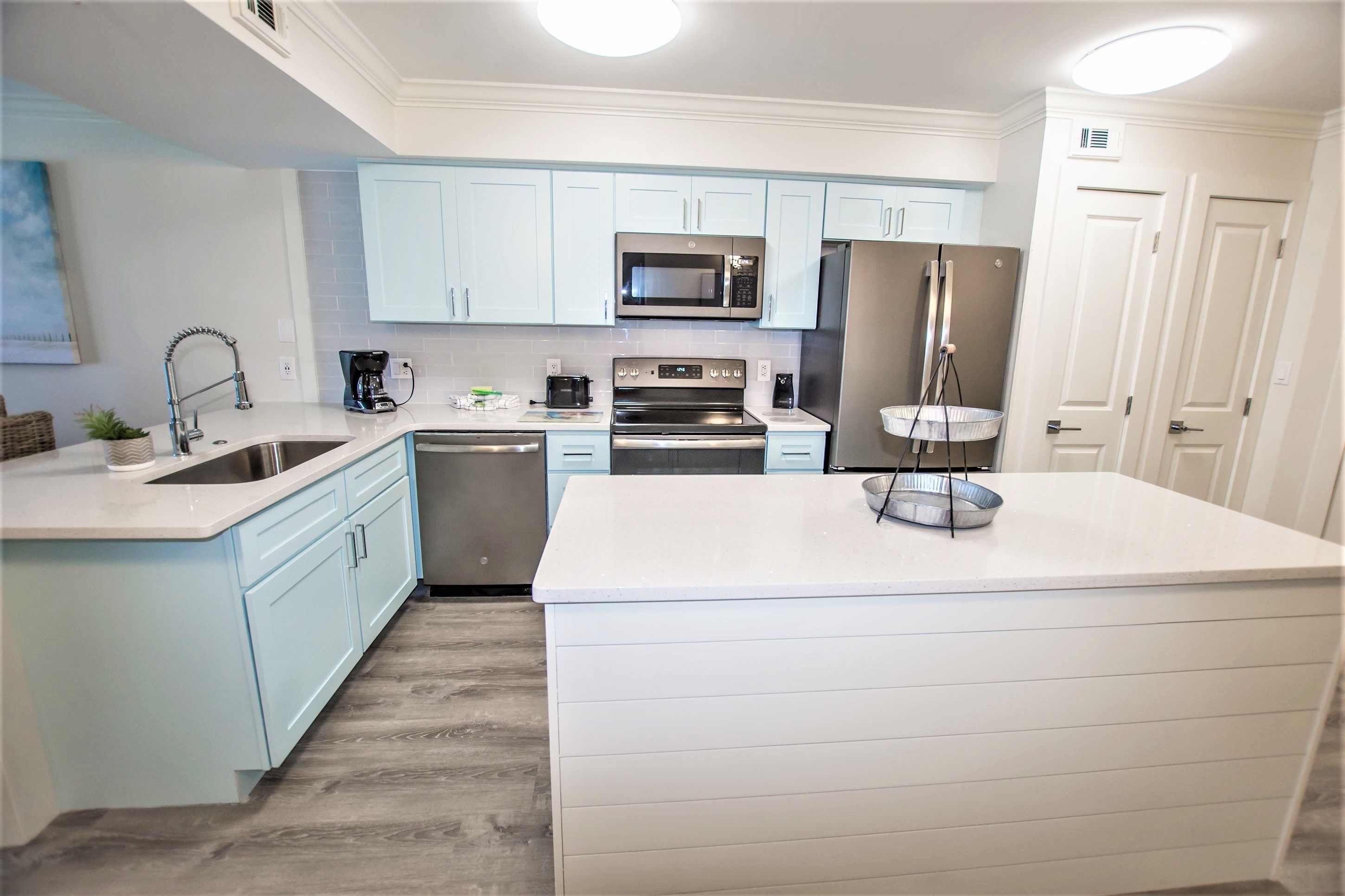 A modern kitchen with light blue cabinets, stainless steel appliances, and a large island.