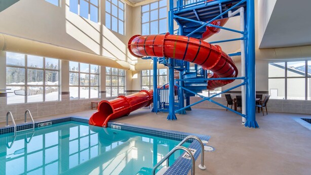 An indoor swimming pool with a red water slide and blue stairs. - Comfort Inn & Suites (Valemount)