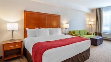 A hotel room with a large bed, a green sofa, a small table, and a nightstand with a lamp.