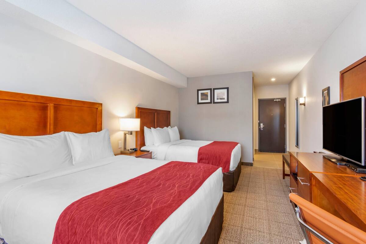 A hotel room with two beds, a TV, a desk, and a door leading to another room.