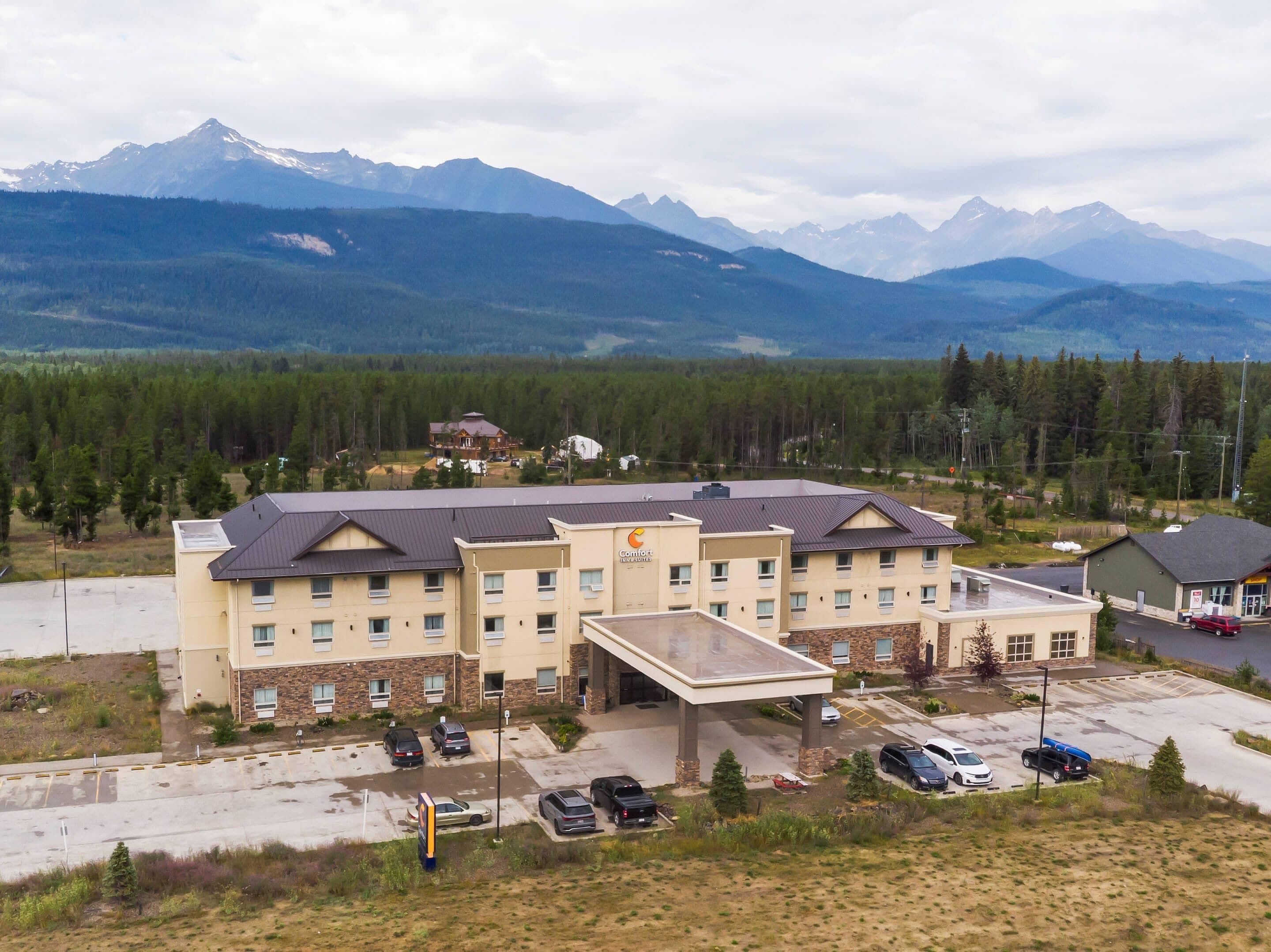 A hotel with a large parking lot, a covered entrance, and a view of mountains in the background.