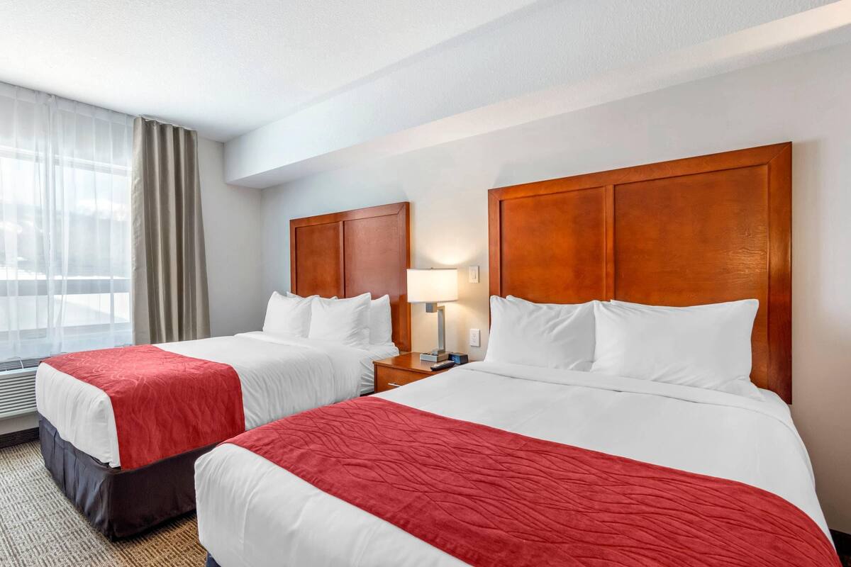 A hotel room with two beds, a nightstand with a lamp, and a window with curtains.