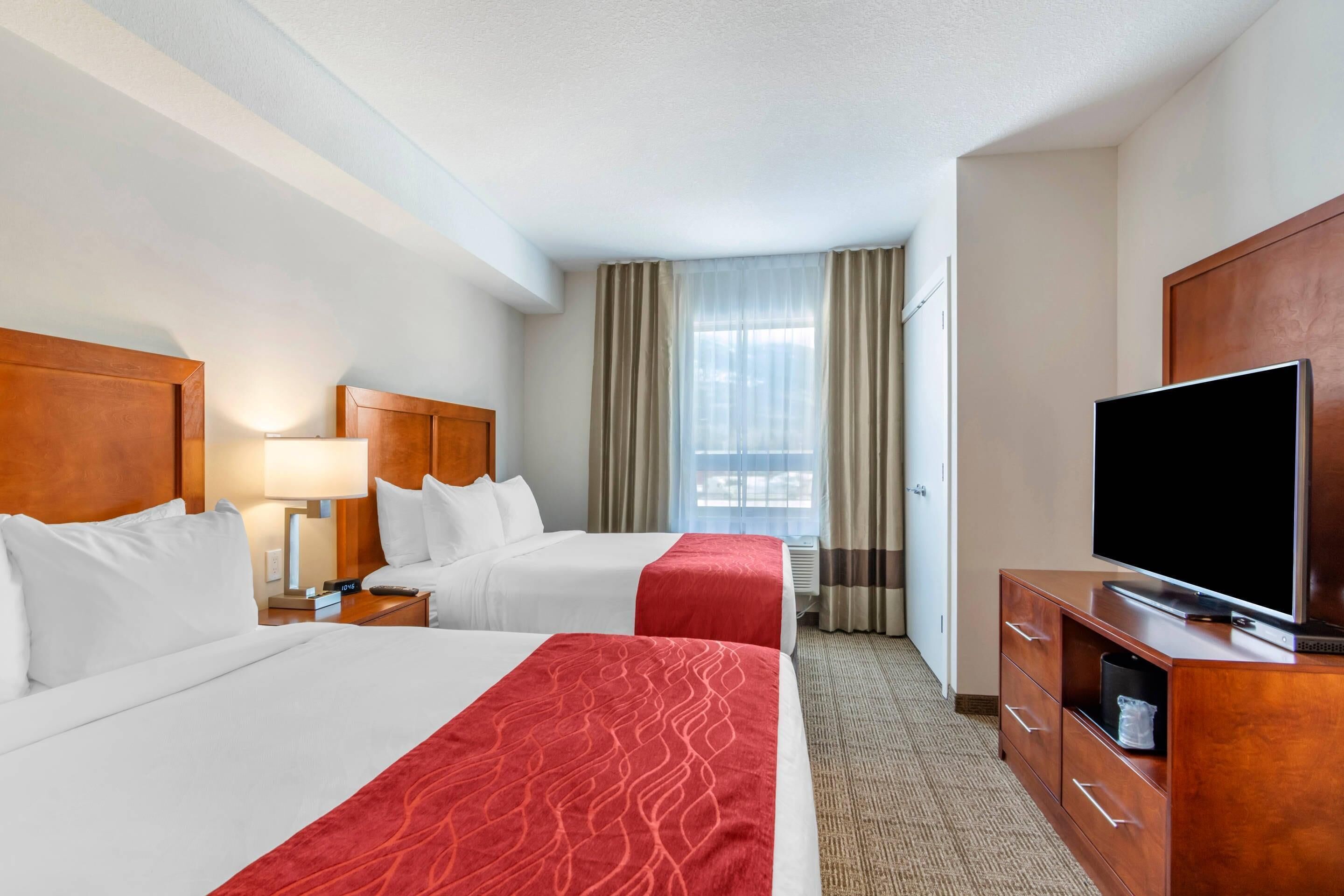 A hotel room with two beds, a TV, a desk, and a window with curtains.