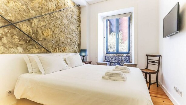 A bedroom with a large bed, a stone wall, a window, a TV, and a chair.