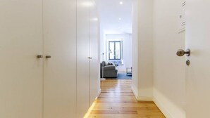 A hallway with wooden flooring leading to a living area with a sofa and a lamp.