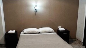 A single bed with a beige blanket, two bedside tables with lamps, and a wall-mounted light fixture. - Hotel Capri (Guatemala City)