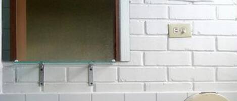 Un baño con pared de azulejos blancos, un espejo con marco de cristal, un lavamanos blanco y un dispensador de toallas de papel.