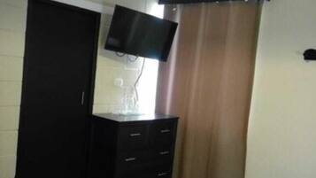 A bedroom with a bed, a dresser, a television on the wall, and a window with curtains.