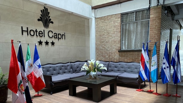 A lobby with a grey sofa, a coffee table with flowers, and multiple flags. - Hotel Capri (Guatemala City)
