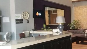 A reception area with a counter, a clock, a TV, and a sofa. - Hotel Capri (Guatemala City)