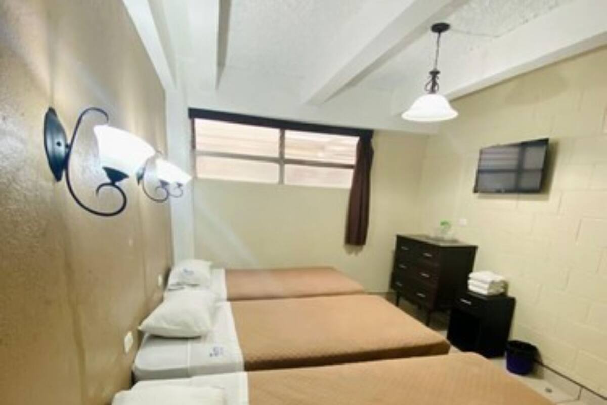 A hotel room with two beds, a dresser, a window, and a wall-mounted TV.