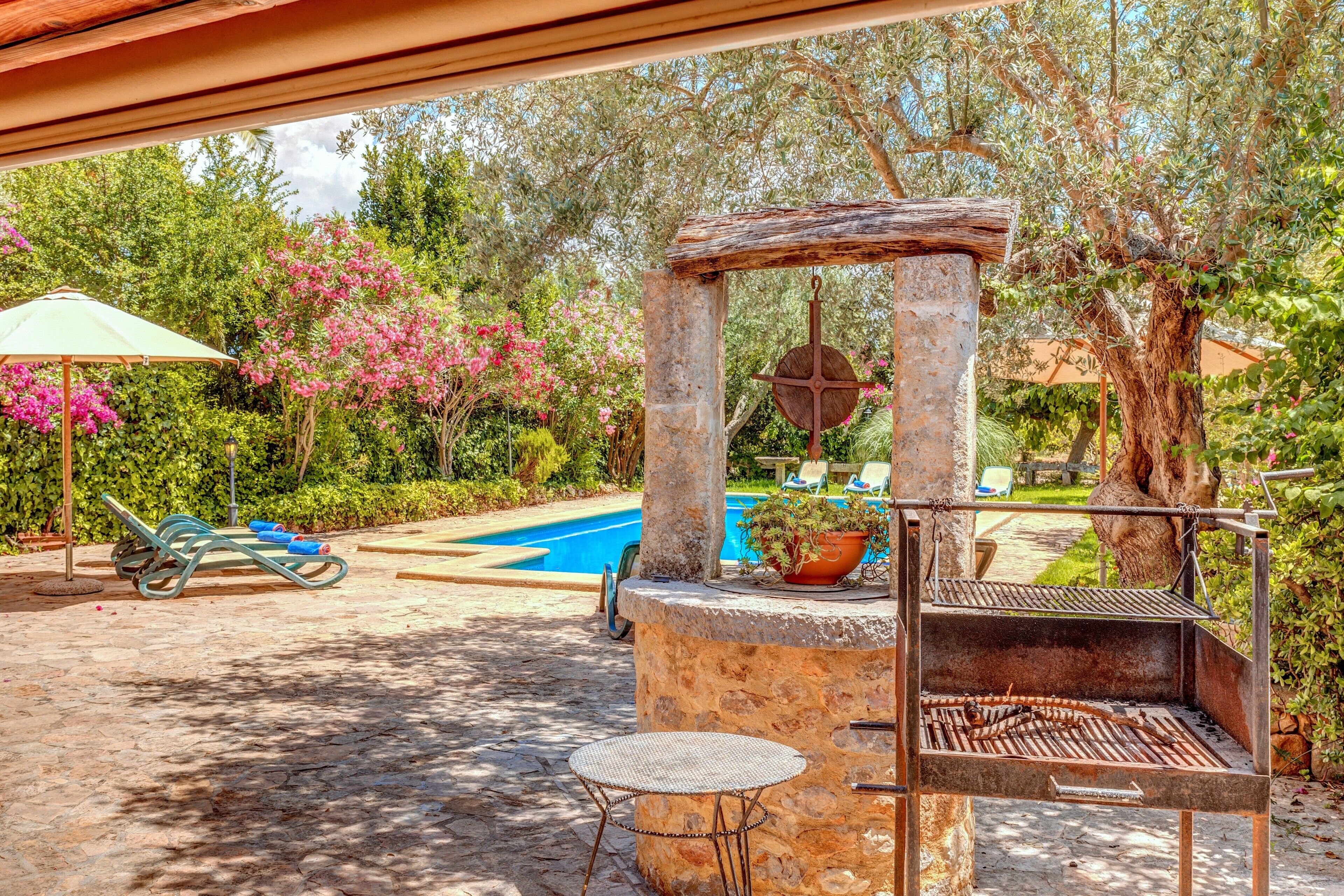 An outdoor barbecue area with a stone grill, a small table, and a pool in the background.
