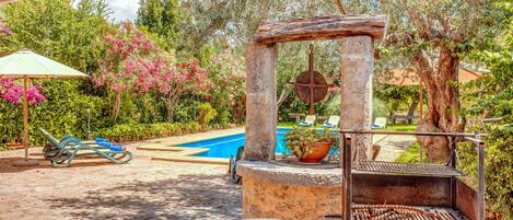 An outdoor barbecue area with a stone grill, a small table, and a pool in the background.