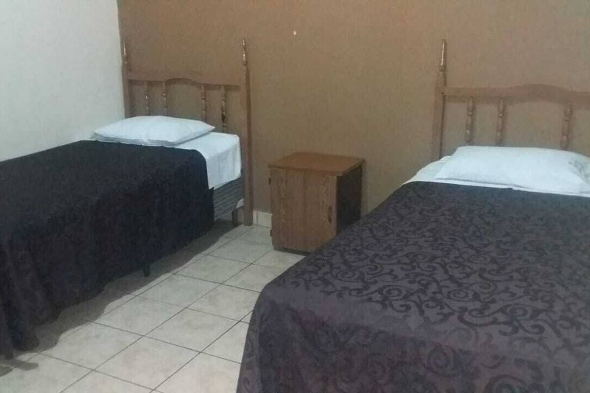 Ein Zimmer mit zwei Einzelbetten, einem Holzkopfteil, einem kleinen Nachttisch und einem gefliesten Boden.