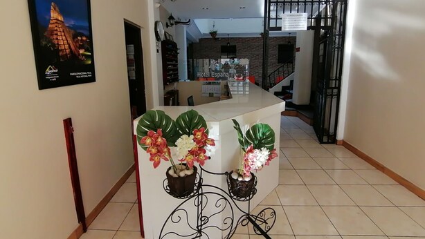 Un vestíbulo de hotel con mostrador de recepción, un cartel de Guatemala y una escalera que sube a otro nivel.