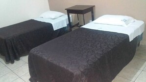 Dos camas individuales con cubrecamas oscuras, una mesita de noche de madera y una pared sencilla.