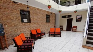 Un espacio interior amplio con piso de baldosas, muebles de madera con cojines anaranjados y una pared de piedra, además de una escalera.