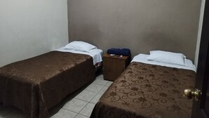 Una habitación pequeña, con poca luz, con dos camas individuales, una mesita de noche de madera y una maleta.