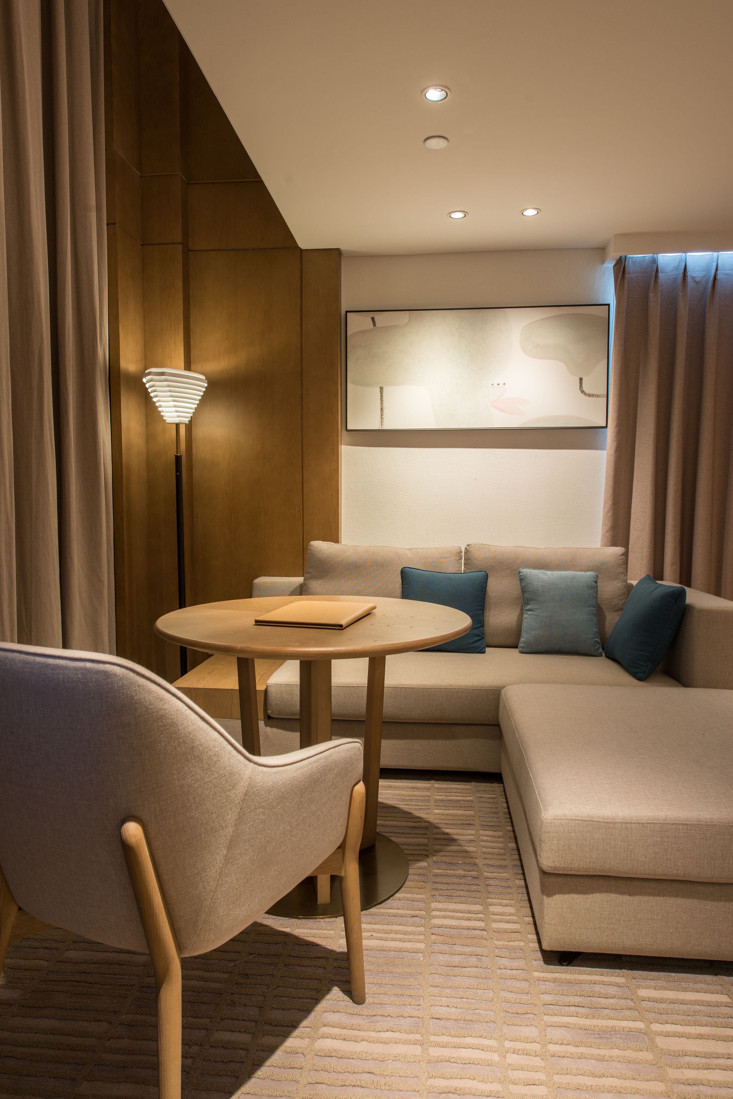 Habitación de hotel moderna con sofá, una mesa redonda, una lámpara y un cuadro abstracto grande en la pared.