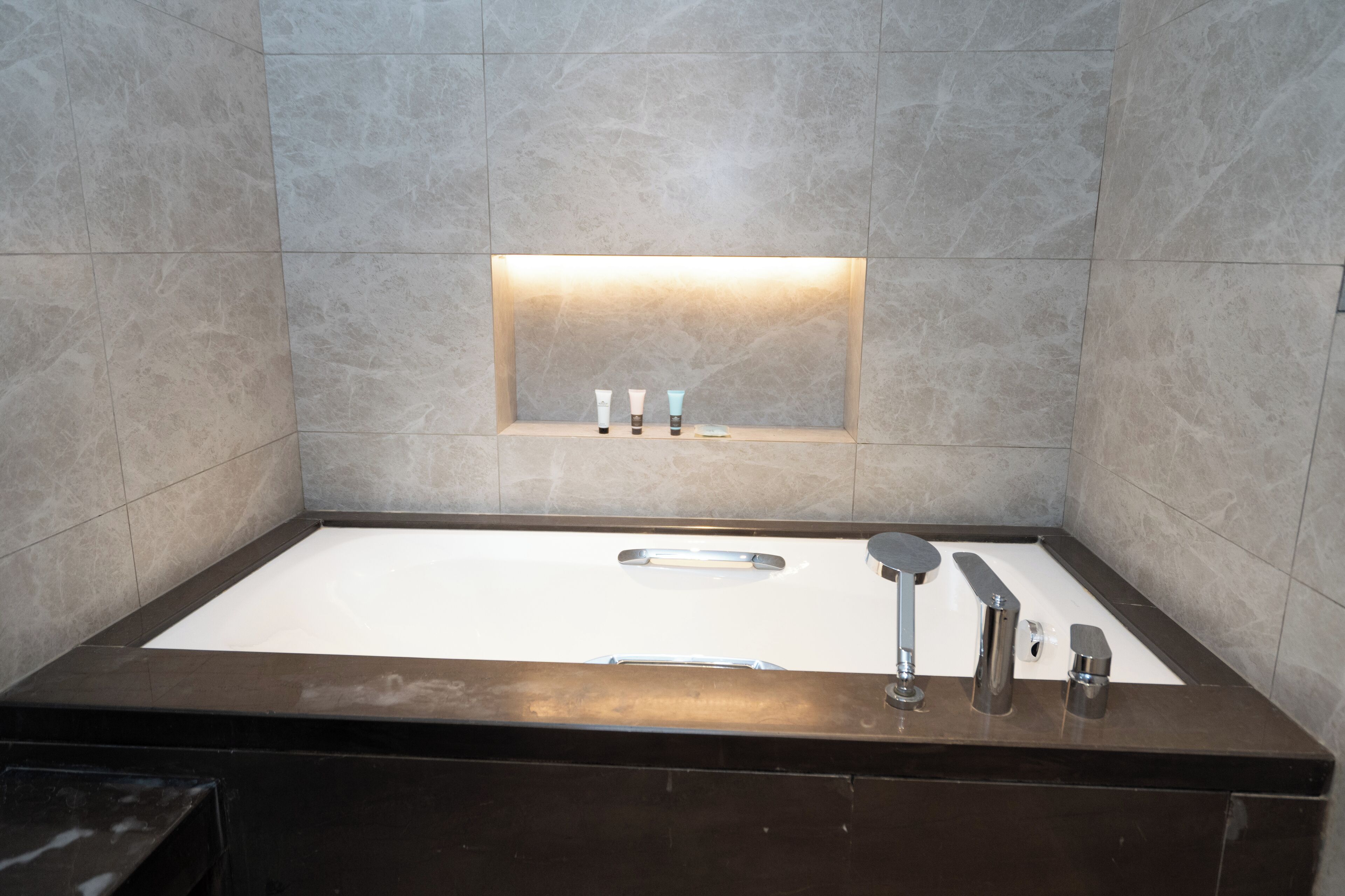 A modern bathroom with a large bathtub, a built-in shelf with toiletries, and a sleek design.