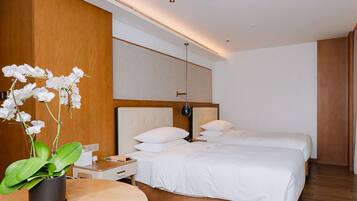 A modern hotel room with two beds, a wooden accent wall, a potted orchid, and a bedside table with a lamp.