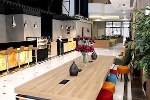 Un vestíbulo de hotel moderno con recepción, zona de bar y asientos.
