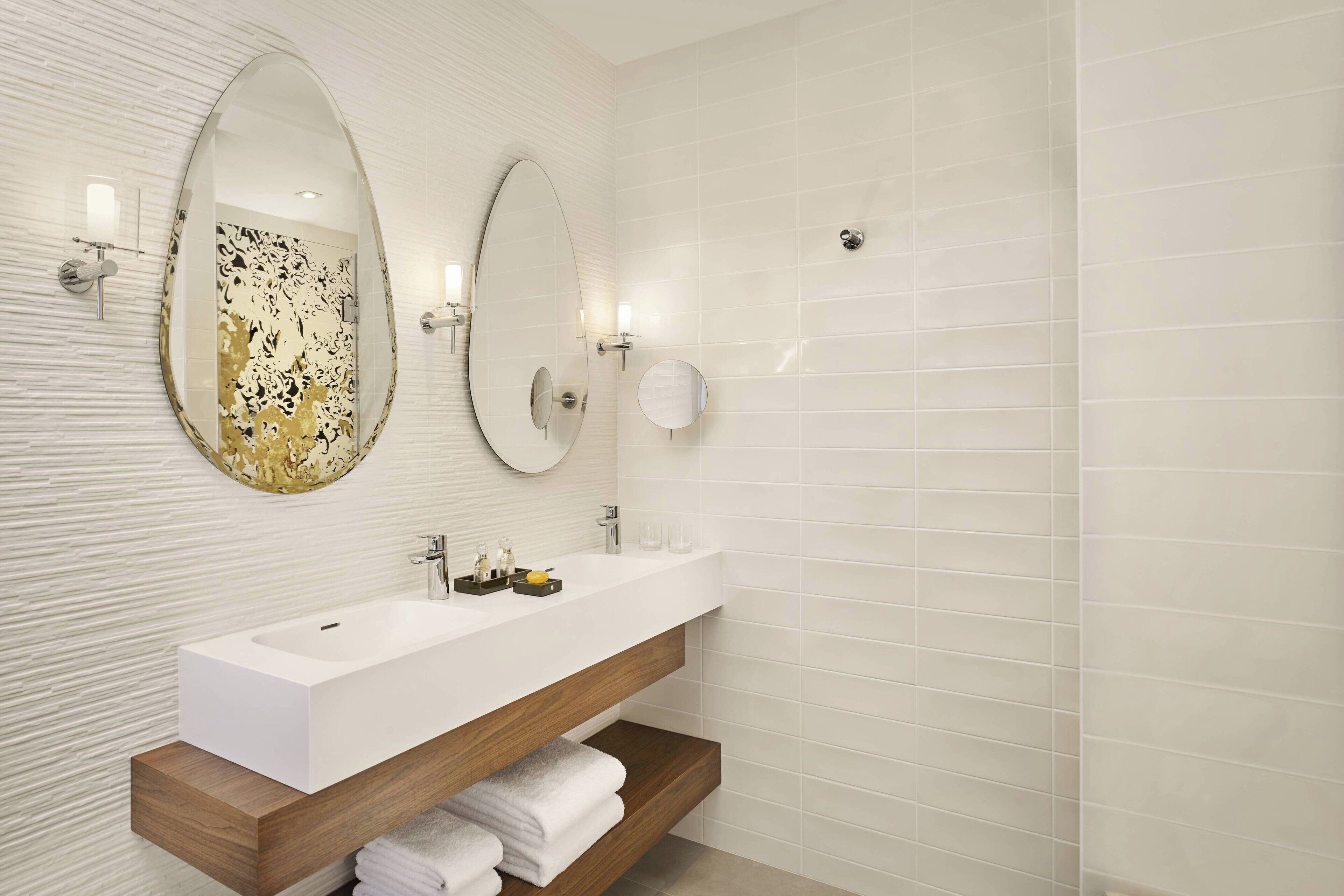 Un baño moderno con un lavabo blanco, dos espejos y un mueble de tocador de madera.