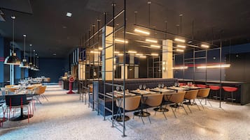 Un interior de restaurante moderno con una larga barra, varias mesas y techos altos con vigas a la vista.