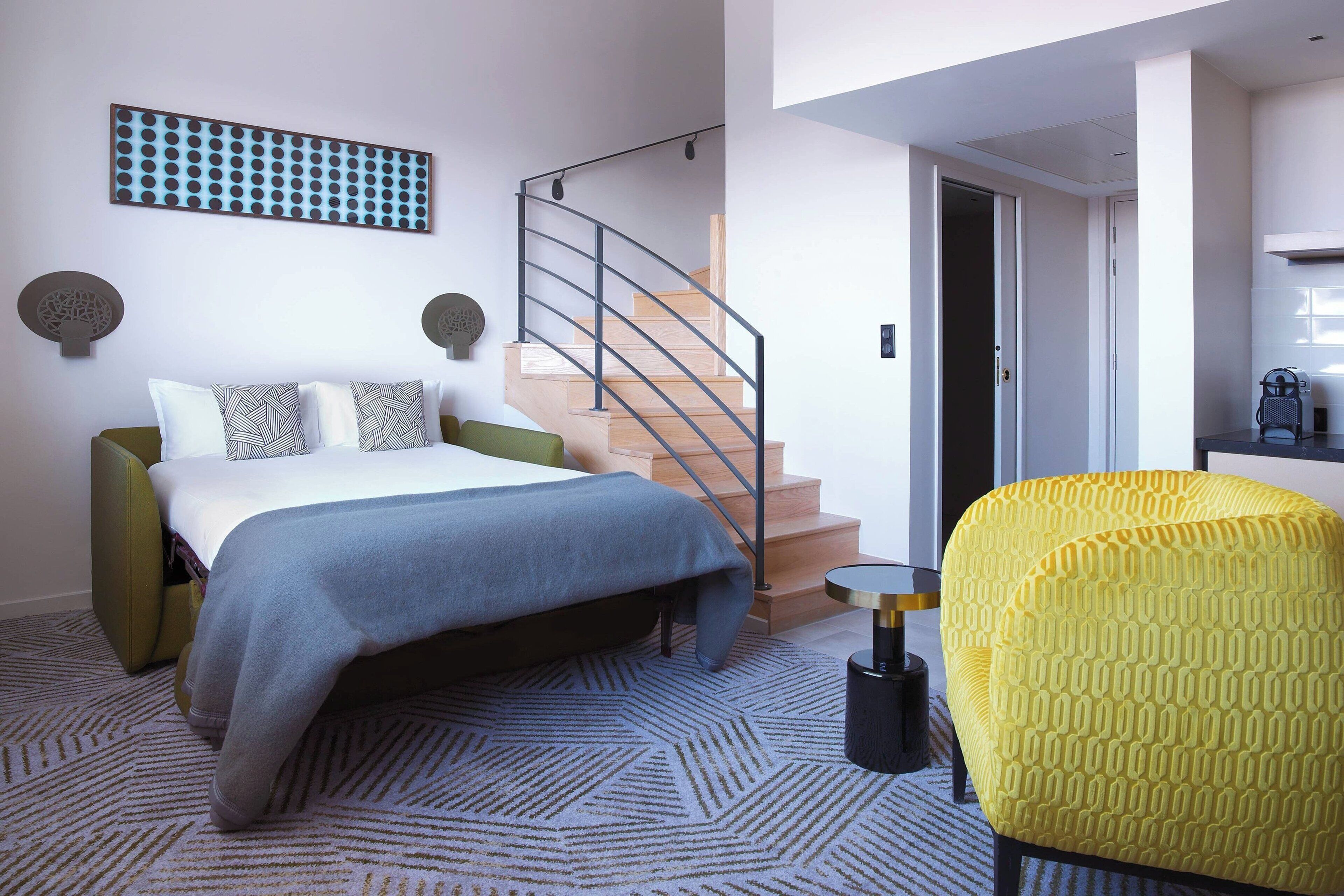 A modern bedroom with a bed, a staircase, and a yellow armchair.