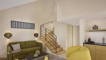 Un salon moderne avec un canapé vert, une petite table ronde et un escalier menant à un espace cuisine.
