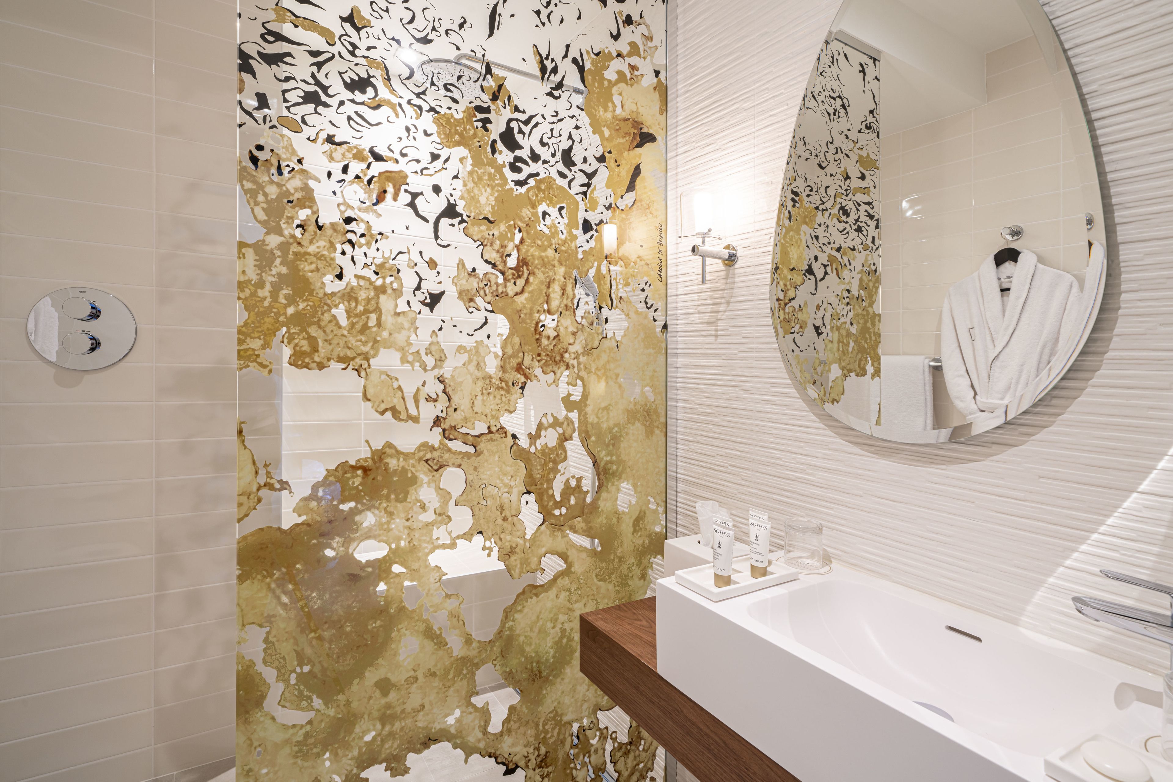 A bathroom with a white sink, a mirror, and a shower area with gold and white patterned tiles.