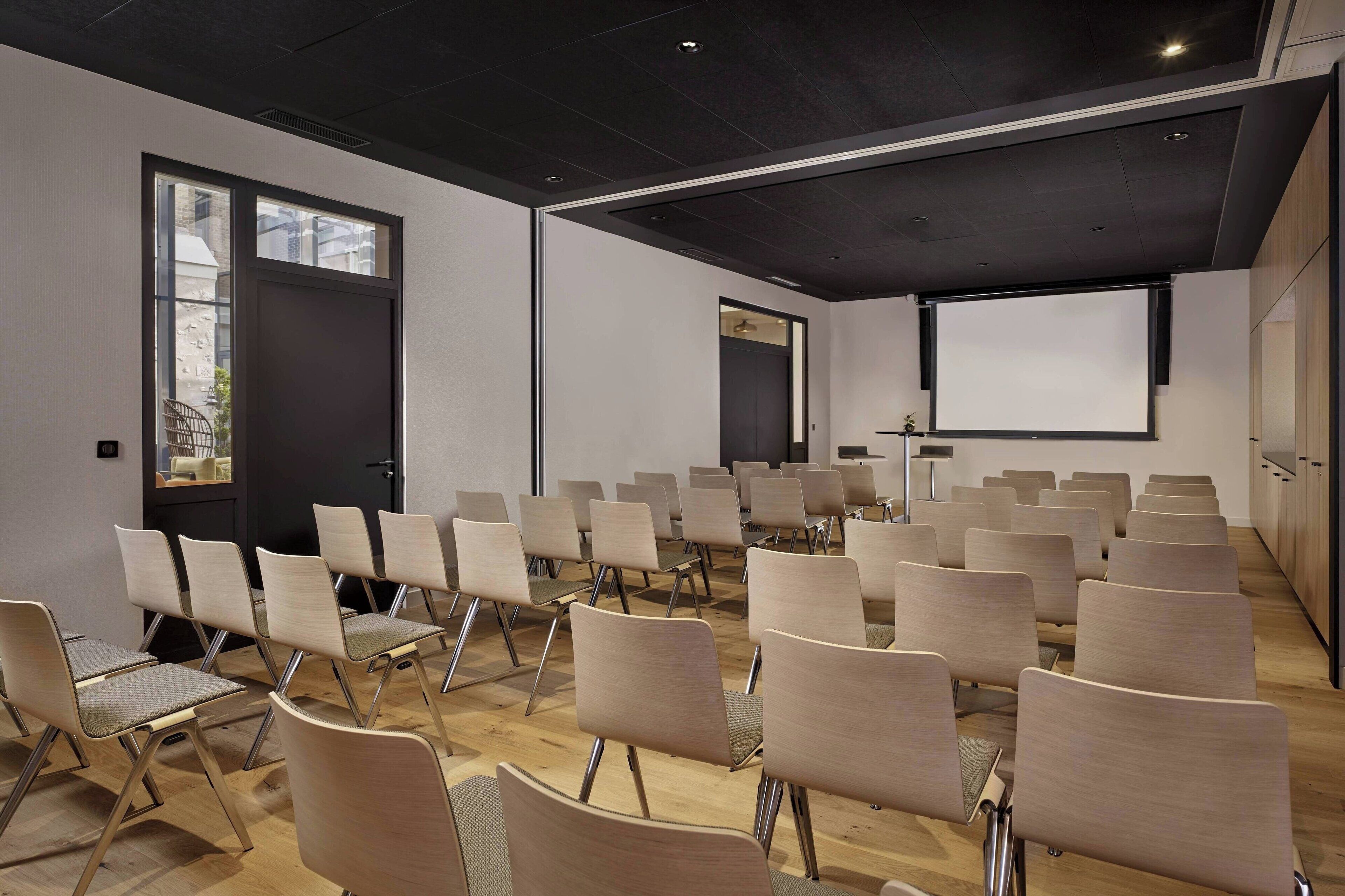 Ein Konferenzraum mit Stuhlreihen, einer Projektionsleinwand und einer Tür.