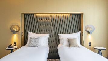 Habitació d'hotel amb dos llits, un reposacapses amb textura, petites làmpades, una taula petita i un telèfon.