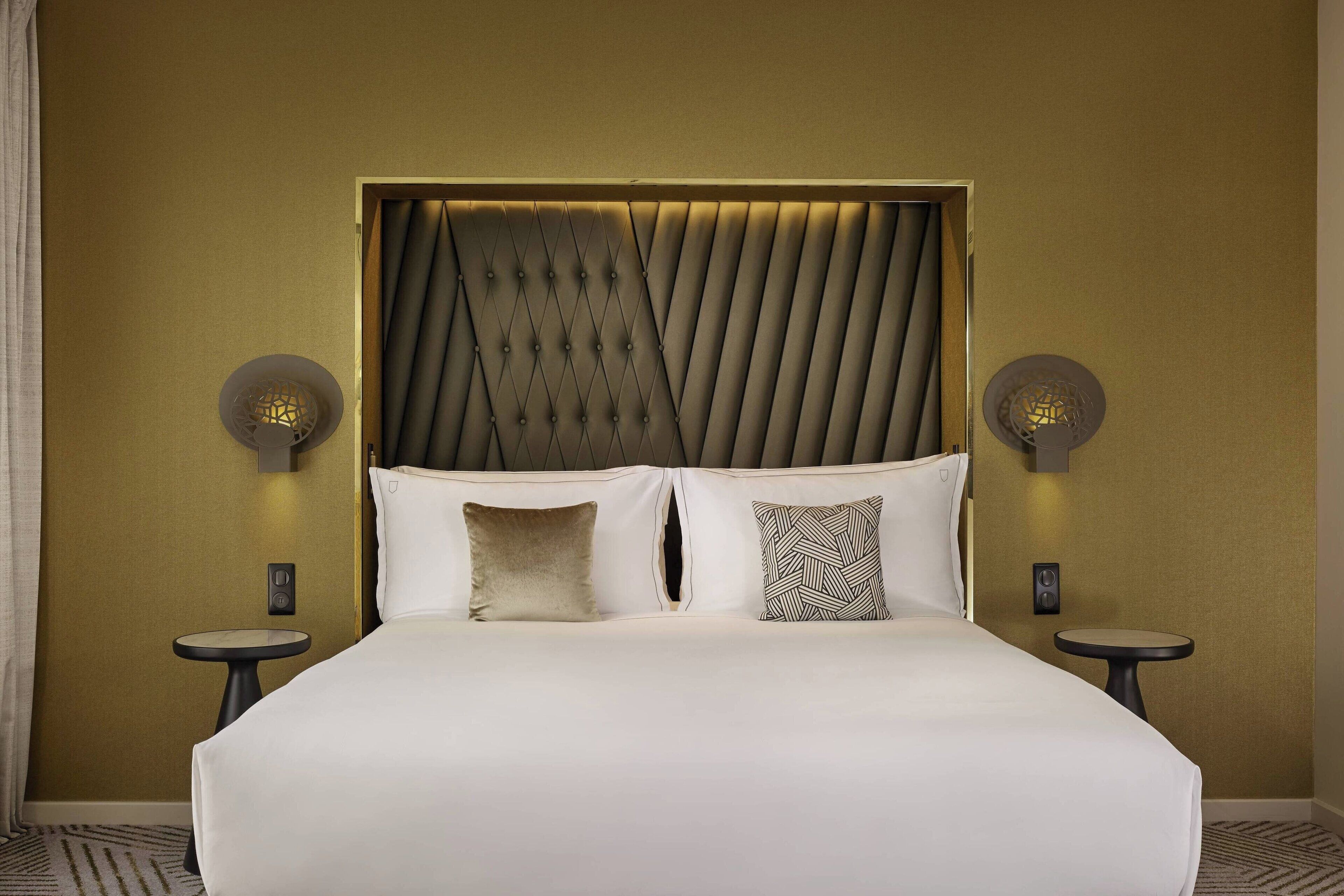 Une chambre d’hôtel dotée d’un grand lit, de deux tables de chevet et d’une tête de lit au design original.