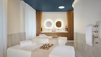 Two large beds with white linens and wooden headboards, a vanity with sink and towel rack, and a small table with a vase of flowers.