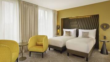 A hotel room with two beds, a yellow armchair, a small round table, and a patterned carpet.