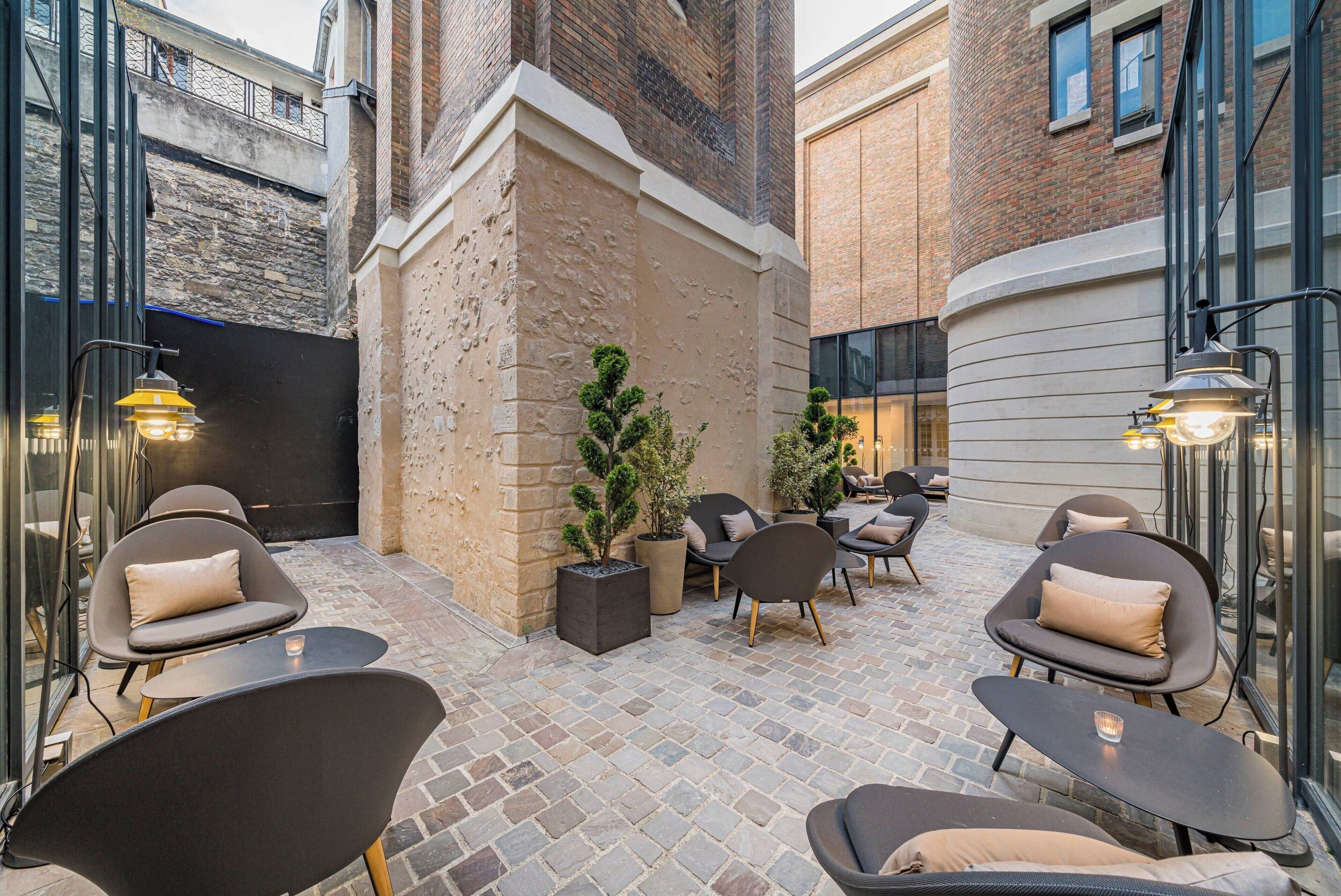 An outdoor seating area with modern chairs and tables, surrounded by brick walls and potted plants.