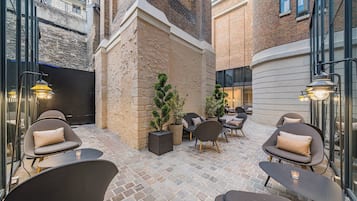 An outdoor seating area with modern chairs and tables, surrounded by brick walls and potted plants.