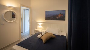A hotel room with a bed, a nightstand, a bedside lamp, a round mirror, and a painting of a cityscape. - B&B Bologna Fair Tower (Bologna)
