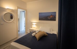 A hotel room with a bed, a nightstand, a bedside lamp, a round mirror, and a painting of a cityscape. - B&B Bologna Fair Tower (Bologna)