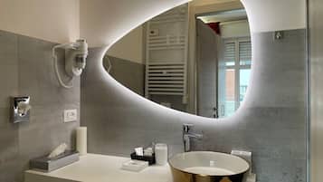 A modern bathroom with a large oval mirror, a round gold sink, a towel dispenser, and a handheld phone.