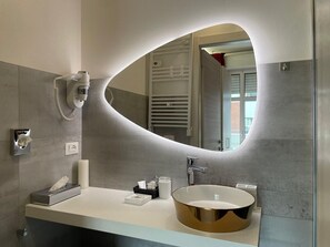 A modern bathroom with a large oval mirror, a round gold sink, a towel dispenser, and a handheld phone. - B&B Bologna Fair Tower (Bologna)