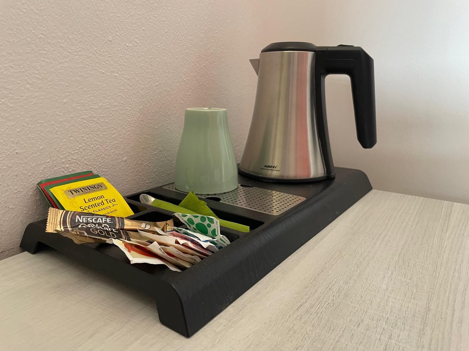 A black tray with a green vase, a silver kettle, and some tea bags.