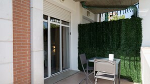 A patio area with a table and chairs, a sliding glass door, and a green artificial hedge. - B&B Bologna Fair Tower (Bologna)