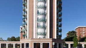 A tall residential building with multiple balconies, a central entrance, and a parking area in front. - B&B Bologna Fair Tower (Bologna)