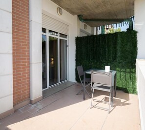 An outdoor patio area with a table and chairs, a sliding glass door, and a green hedge. - B&B Bologna Fair Tower (Bologna)