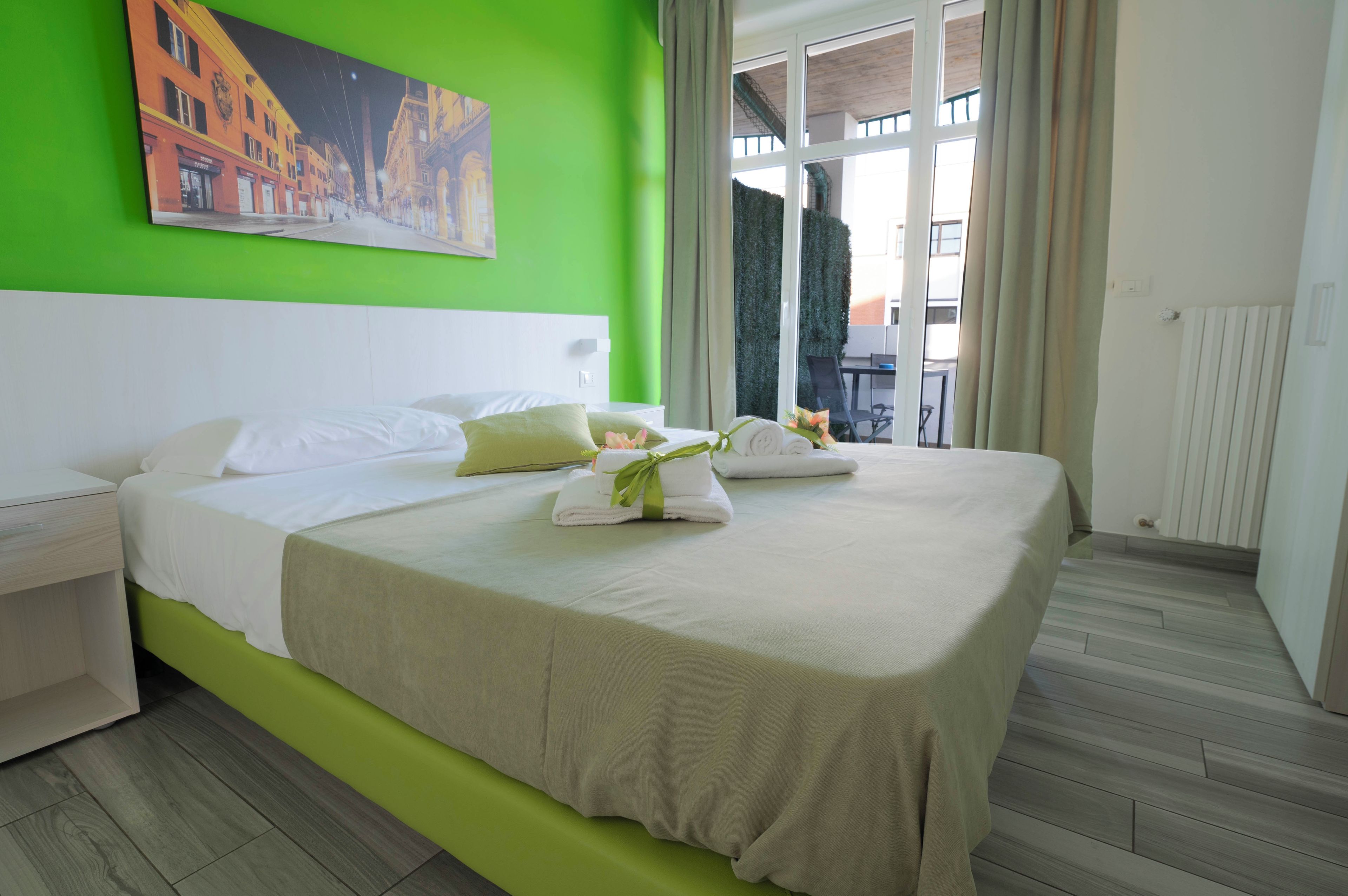 Ein Hotelzimmer mit einem großen Bett, einer grünen Akzentwand und einem Gemälde einer Straßenszene.