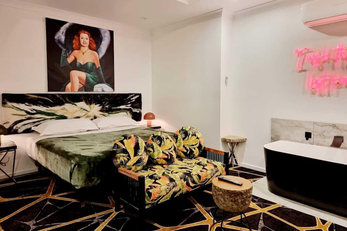 A modern bedroom with a bed, a sofa, a nightstand, and a neon sign.