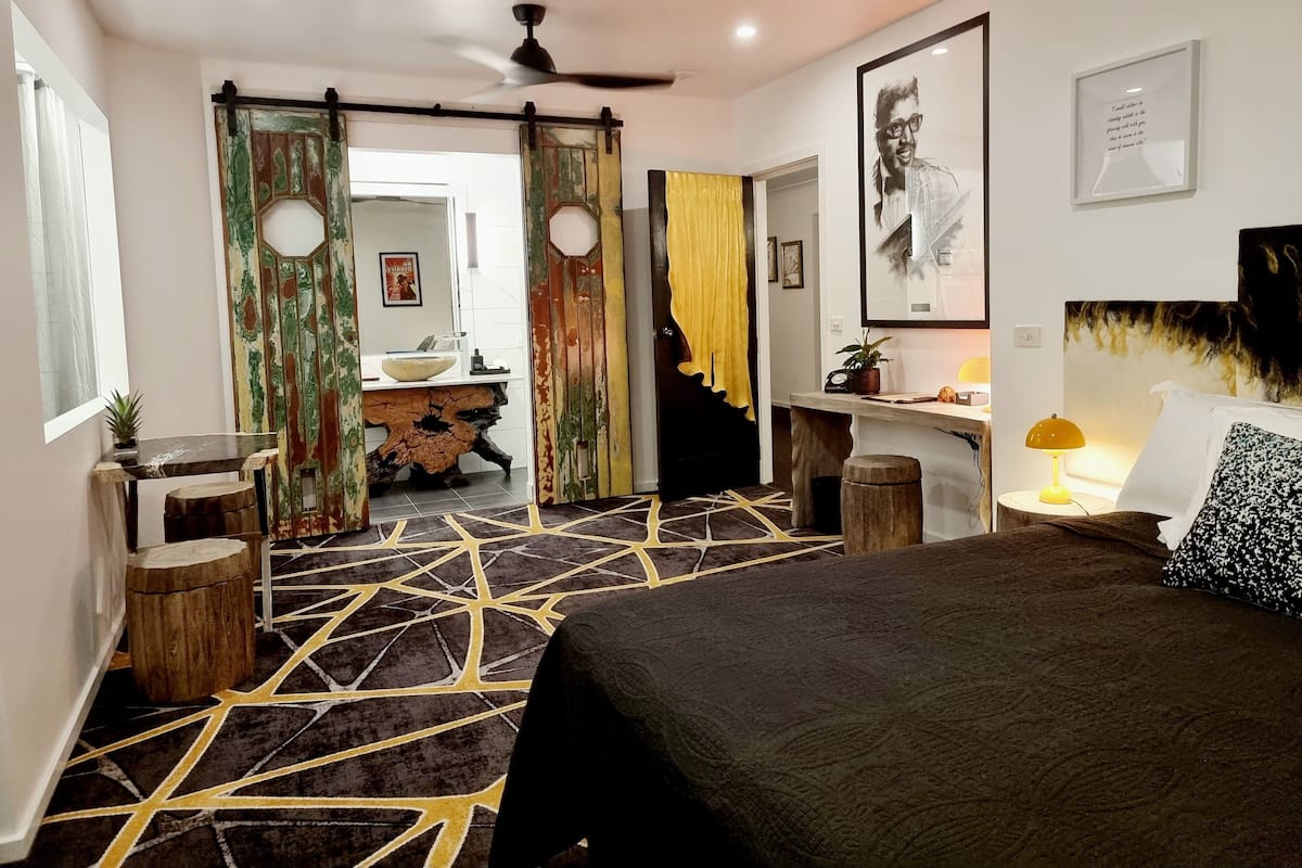 A bedroom with a bed, a desk, a chair, a ceiling fan, and a door with curtains.